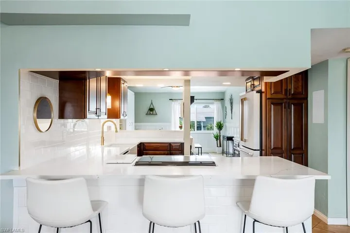 Kitchen featuring a peninsula, high end white refrigerator, a breakfast bar area, backsplash, and black electric stovetop