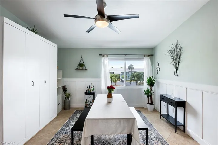 Dining area with wainscoting, a decorative wall, a ceiling fan, and light tile patterned floors