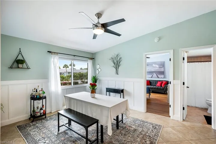 Dining area with a wainscoted wall, a ceiling fan, a decorative wall, and light tile patterned floors