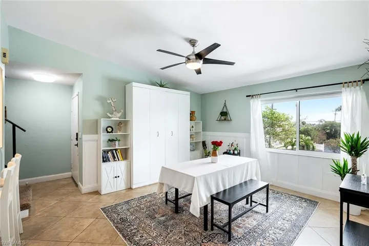 Dining room featuring vaulted ceiling, ceiling fan, a wainscoted wall, and light tile patterned flooring