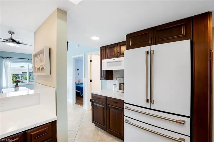 Kitchen featuring dark wood finish cabinets, white appliances, light tile patterned floors, light stone countertops, and recessed lighting