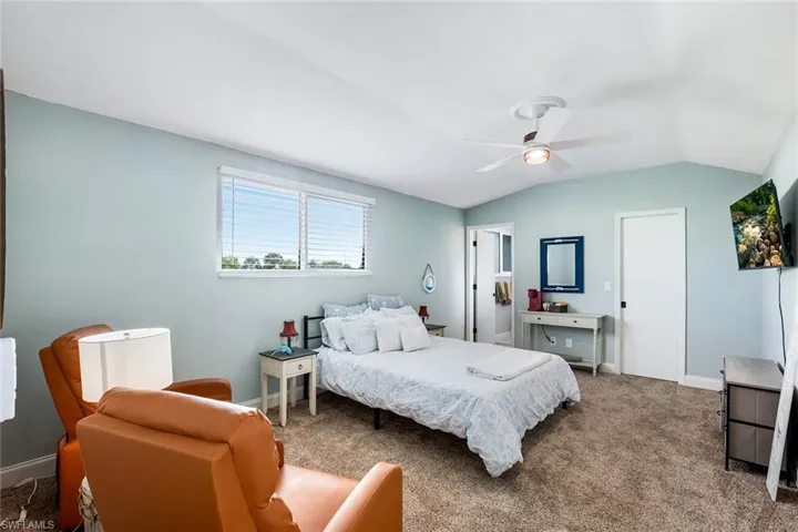 Carpeted bedroom featuring ceiling fan and vaulted ceiling