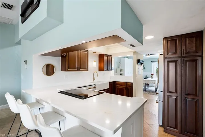Kitchen with a peninsula, a kitchen breakfast bar, light countertops, light tile patterned flooring, and stainless steel fridge