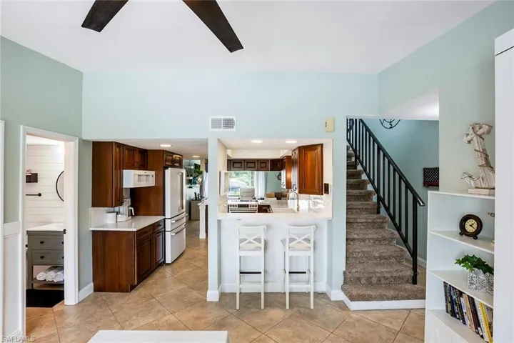 Kitchen with a kitchen bar, premium appliances, a ceiling fan, dark wood finish cabinetry, and a peninsula
