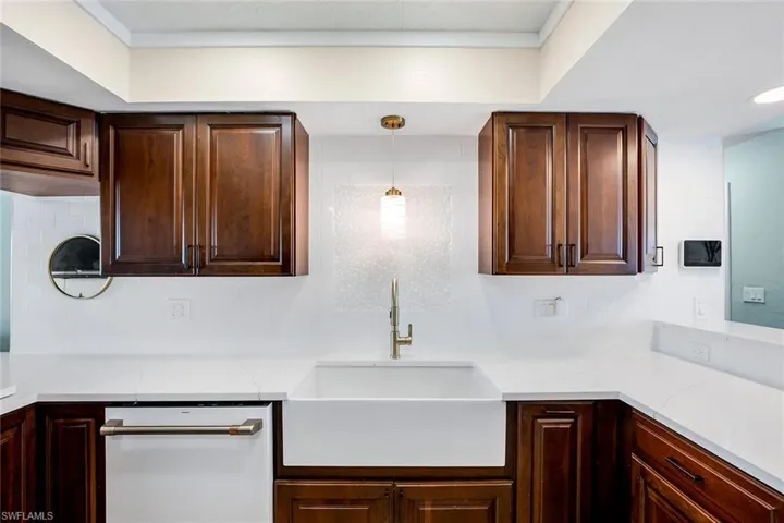 Kitchen featuring white dishwasher, backsplash, dark wood finish cabinetry, light stone counters, and crown molding