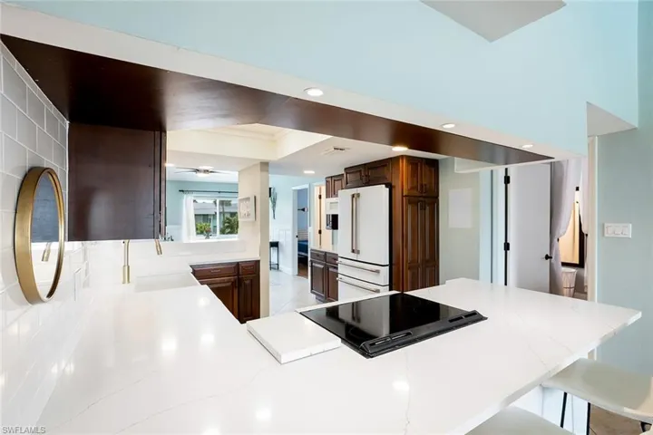 Kitchen with high end white fridge, black electric stovetop, a kitchen breakfast bar, and dark wood finish cabinets