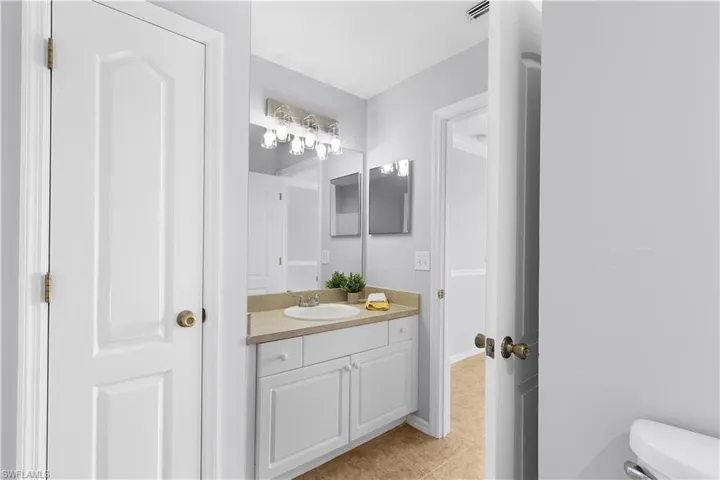 Elegant bathroom vanity featuring white cabinetry with a wood-finish countertop, dual mirrors with integrated lighting, and brushed brass hardware