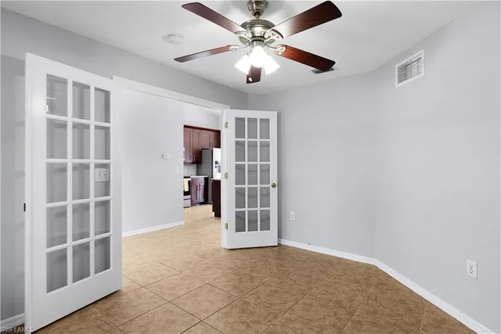 French doors with glass panes, ceiling fan with integrated lighting, tile flooring, and light-toned wall finishes