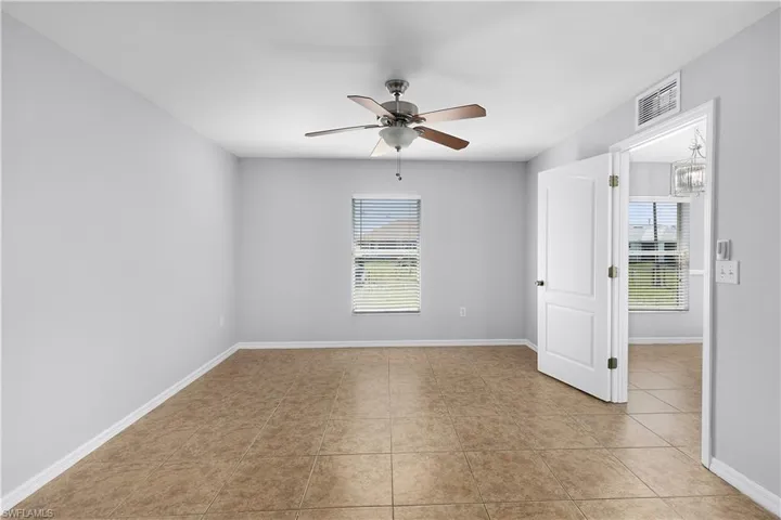 Neutral wall paint, tile flooring, window with blinds, ceiling fan with integrated lighting, and a paneled door