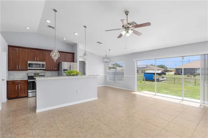 Vaulted ceilings over a kitchen with wood cabinetry, stainless steel appliances, and a tiled backsplash
