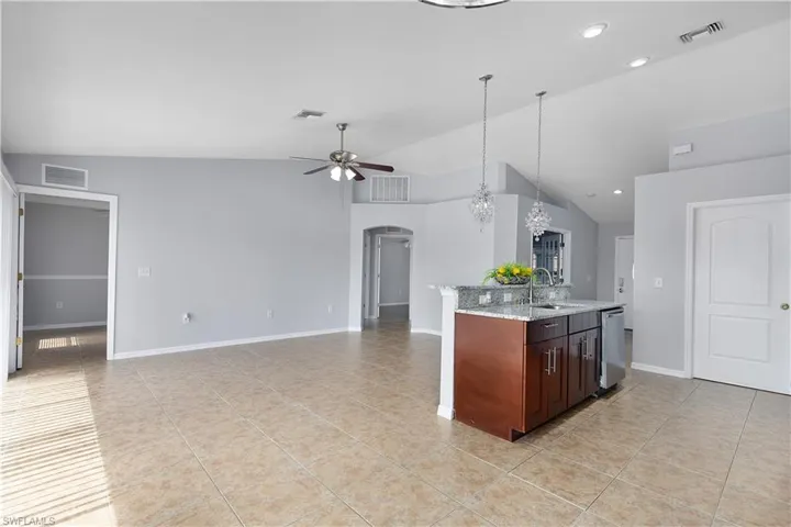 Open-concept living area featuring tile flooring, vaulted ceilings, and a kitchen island with granite countertops
