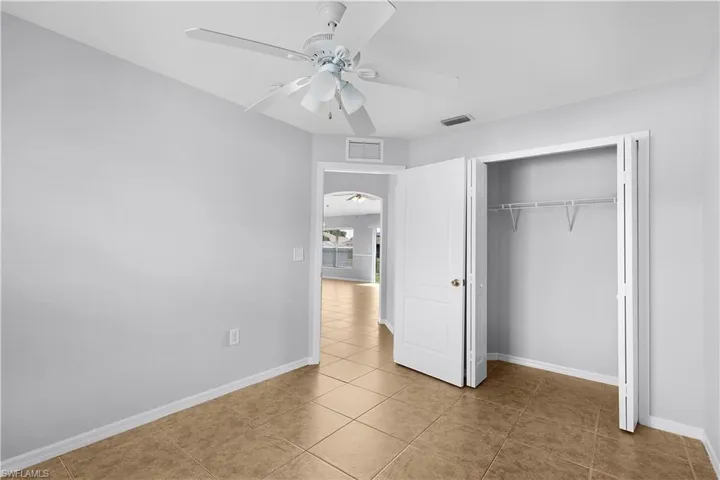 Tile flooring with a neutral finish, a built-in closet with bifold doors, and a ceiling fan with integrated lighting