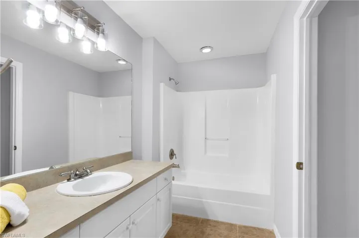Bathroom featuring a white bathtub/shower combination, vanity with an integrated sink, broad mirror, and a modern light fixture