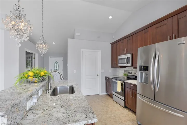 Kitchen featuring granite countertops, stainless steel appliances, wood cabinetry, tile flooring, and vaulted ceiling