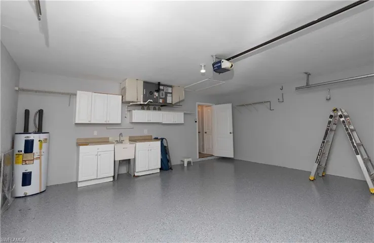 Spacious garage with epoxy-coated flooring, white cabinetry, utility sink, and overhead storage system