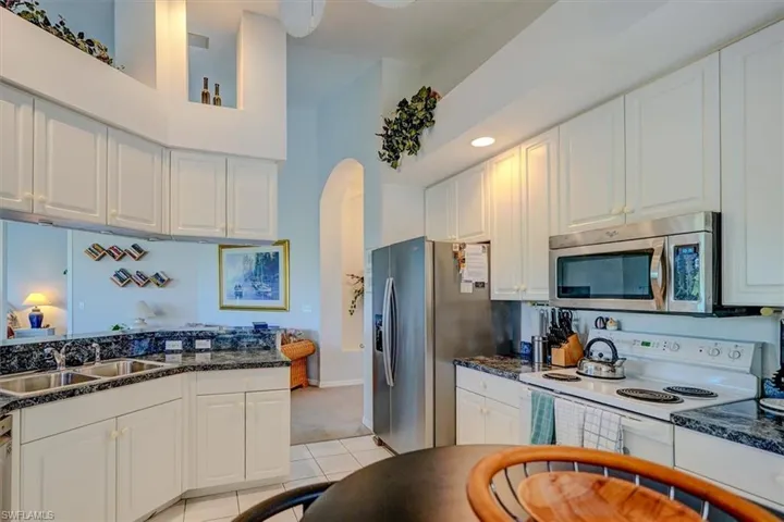 Kitchen with appliances with stainless steel finishes, white cabinets, arched walkways, light carpet, and light tile patterned floors