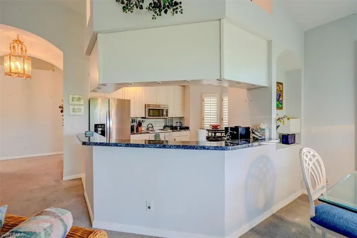 Kitchen with stainless steel appliances, arched walkways, a chandelier, light colored carpet, and a towering ceiling