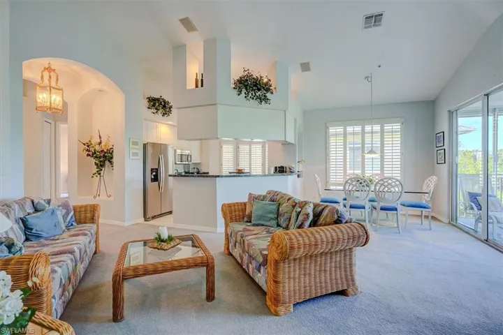 Living area featuring light colored carpet, a chandelier, vaulted ceiling, and arched walkways