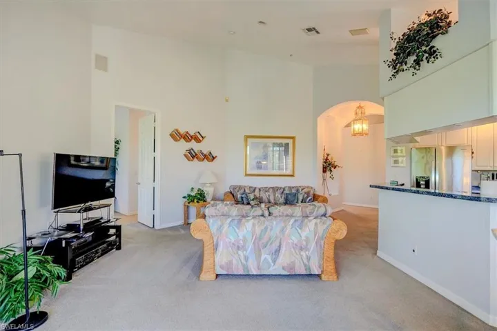 Living area with a towering ceiling, light colored carpet, and arched walkways