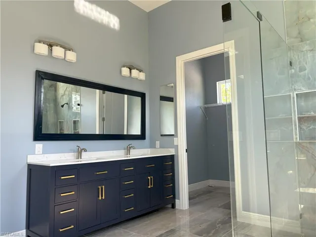Bathroom featuring double vanity, a stall shower, light marble finish floors, and a spacious closet