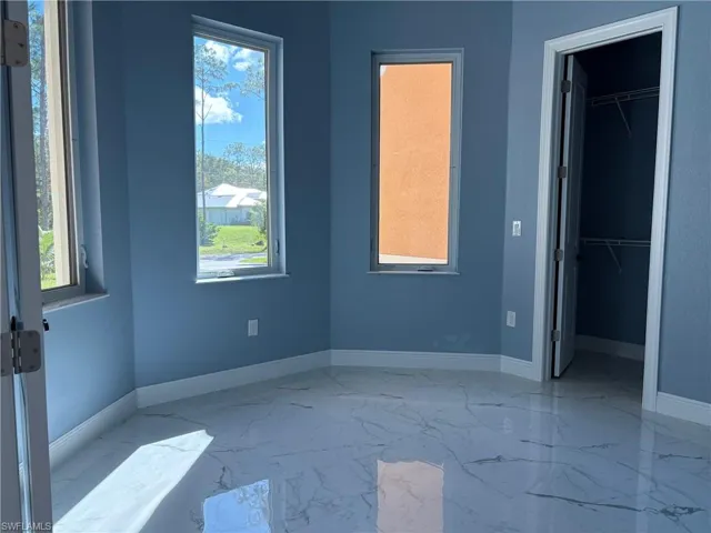 Unfurnished bedroom featuring a walk in closet and light marble finish floors