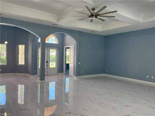 Unfurnished room with light marble finish floors, ornamental molding, arched walkways, coffered ceiling, and ceiling fan