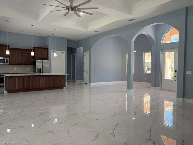 Unfurnished living room featuring coffered ceiling, beam ceiling, a towering ceiling, arched walkways, and light marble finish flooring