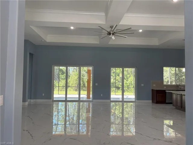 Empty room featuring light marble finish floors, coffered ceiling, beamed ceiling, a ceiling fan, and crown molding