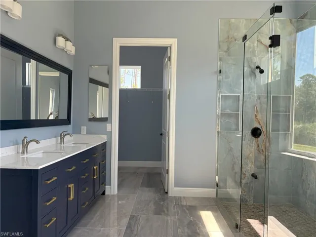 Bathroom featuring a marble finish shower, double vanity, dark marble finish flooring, and a closet