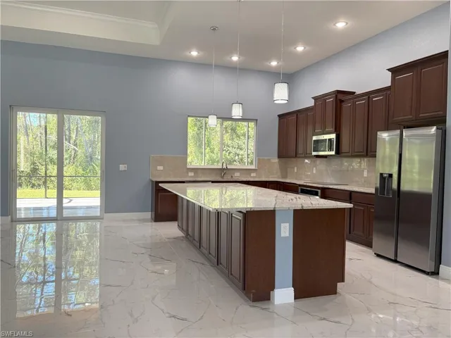 Kitchen with stainless steel appliances, light marble finish flooring, a kitchen island, light stone counters, and recessed lighting