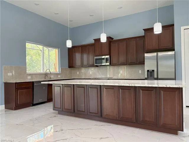 Kitchen with appliances with stainless steel finishes, light marble finish floors, tasteful backsplash, a large island, and light stone counters
