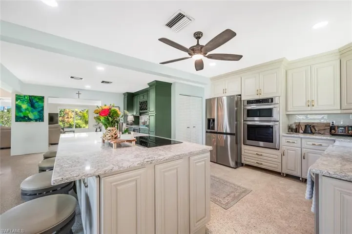Kitchen featuring light stone counters, a kitchen island with sink, stainless steel appliances, and a kitchen bar