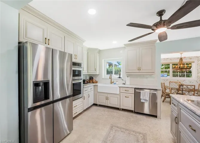 Kitchen with cream cabinets, sink, stainless steel appliances, light stone countertops, and ceiling fan with notable chandelier