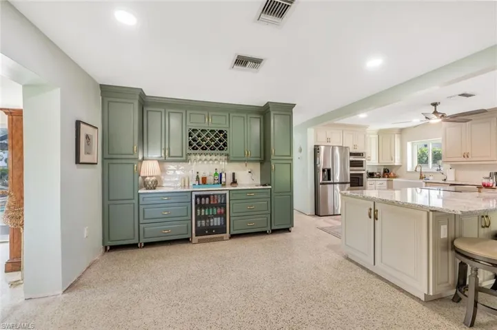 Kitchen featuring appliances with stainless steel finishes, a kitchen breakfast bar, light stone counters, decorative backsplash, and beverage cooler