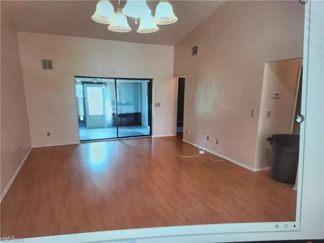 Spare room with hanging lights, wood finished floors, and vaulted ceiling