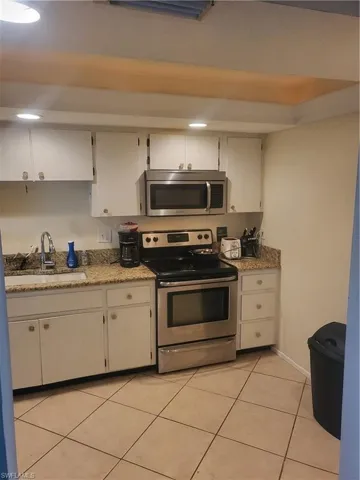 Kitchen with stainless steel appliances, light tile patterned flooring, light stone counters, white cabinets, and recessed lighting