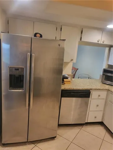 Kitchen featuring appliances with stainless steel finishes, light tile patterned flooring, and white cabinets