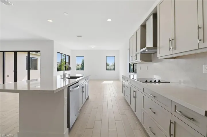 Kitchen with light stone countertops, recessed lighting, a center island with sink, wall chimney range hood, and dishwasher