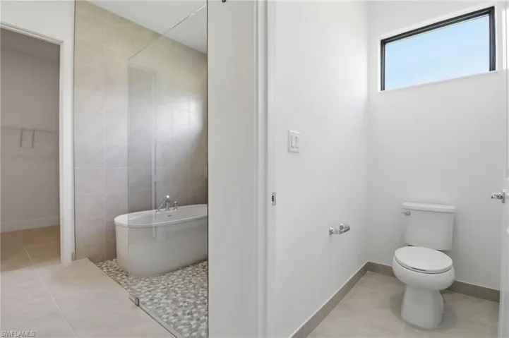 Bathroom featuring light tile patterned flooring, tile walls, a freestanding tub, and a walk in closet