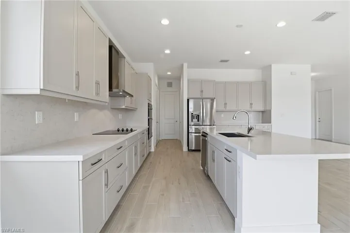 Kitchen featuring tasteful backsplash, stainless steel refrigerator with ice dispenser, a kitchen island with sink, wall chimney range hood, and recessed lighting