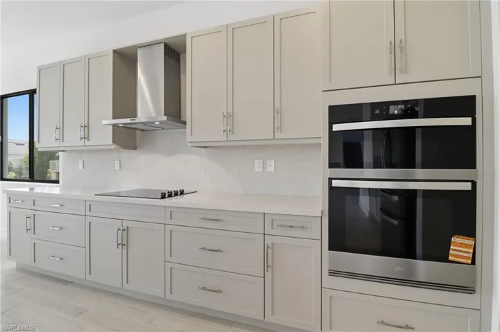 Kitchen featuring double oven, wall chimney exhaust hood, light stone counters, decorative backsplash, and black electric cooktop
