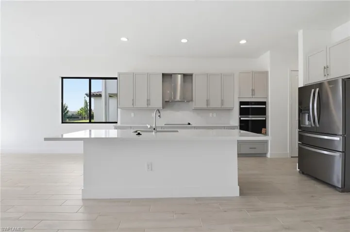 Kitchen with stainless steel refrigerator with ice dispenser, a kitchen island with sink, light stone countertops, wood finish floors, and wall chimney exhaust hood
