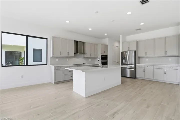 Kitchen featuring gray cabinets, appliances with stainless steel finishes, a center island with sink, decorative backsplash, and recessed lighting