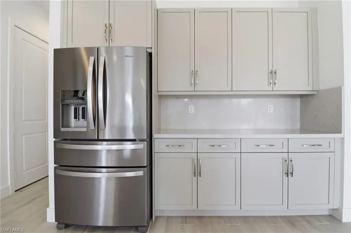 Kitchen with stainless steel refrigerator with ice dispenser, decorative backsplash, wood tiled floors, and light stone counters
