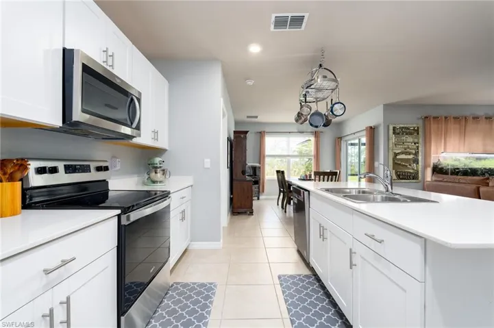 Kitchen with stainless steel appliances, white cabinetry, center island with quartz countertops and stainless double bowl sink