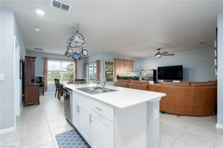 Kitchen with white cabinetry, light countertops, open floor plan, light tile patterned floors, and a kitchen island with sink and pot hangers