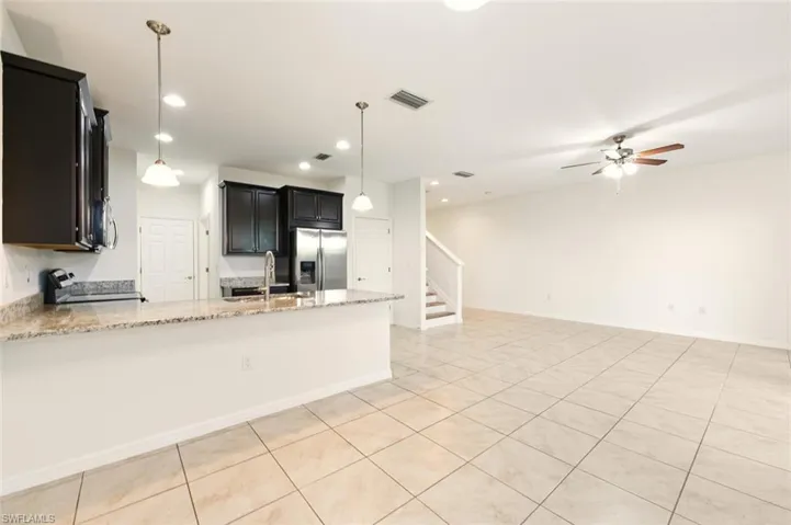 Kitchen with light stone countertops, decorative light fixtures, a peninsula, black electric range, and stainless steel fridge with ice dispenser