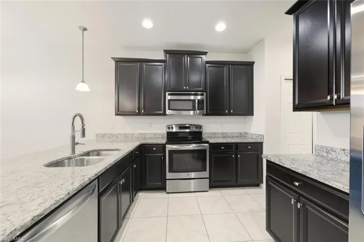 Kitchen with light stone counters, dark cabinets, appliances with stainless steel finishes, and recessed lighting