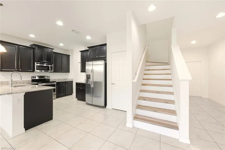 Kitchen with dark cabinets, stainless steel appliances, light stone countertops, light tile patterned floors, and recessed lighting