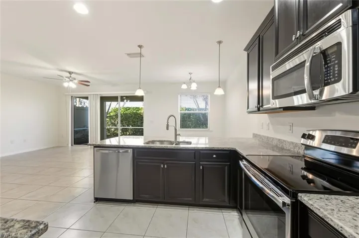 Kitchen featuring appliances with stainless steel finishes, pendant lighting, light stone countertops, dark cabinetry, and open floor plan